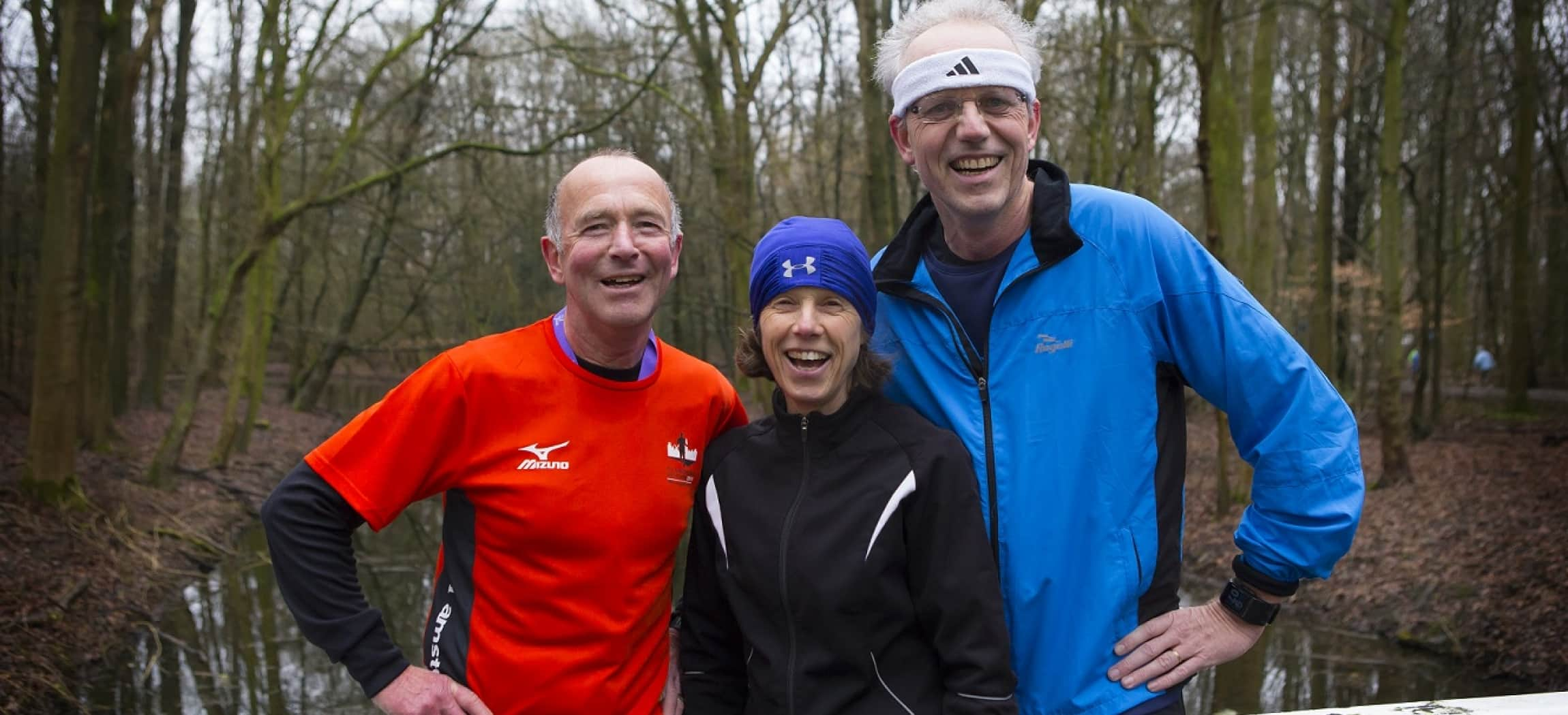 Drie sportieve mensen in sportkleding staan in een bos