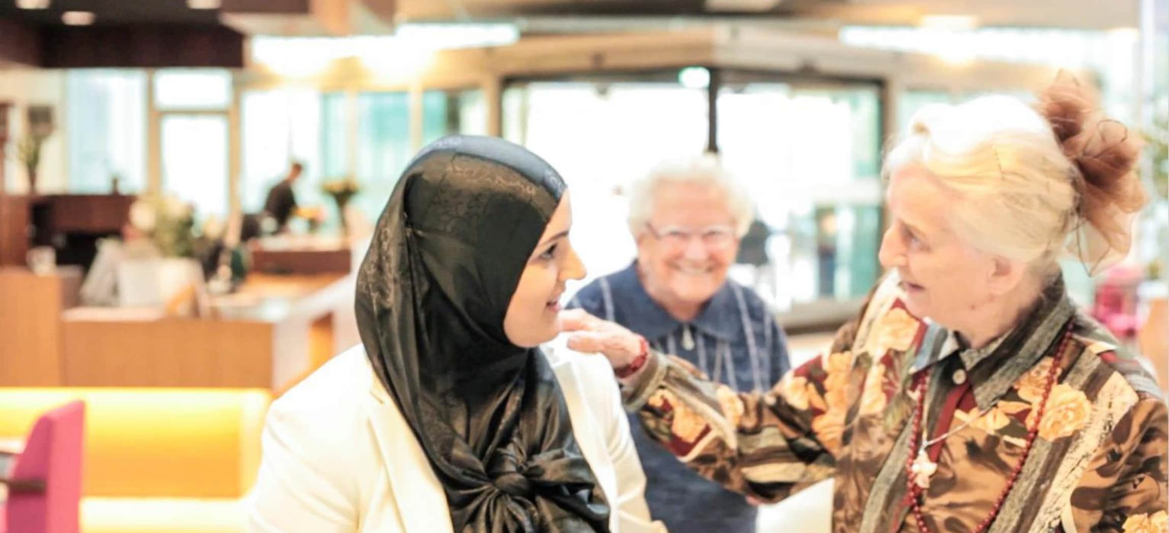 Oudere vrouwen praten enthousiast met jongere vrouw met zwarte hoofddoek of hijab