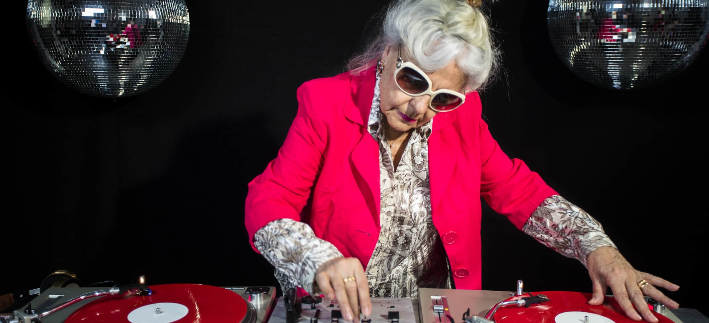 Hippe oudere vrouw aan draaitafel mixt muziek tijdens dansfeest voor swingende senioren