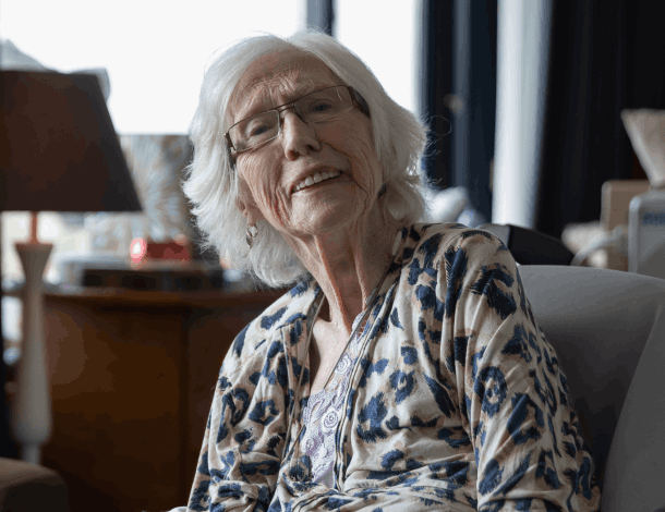 Verzorgende met krullend haar geeft oude vrouw drinken met rietje